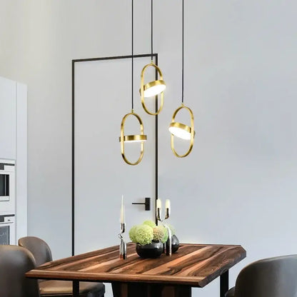 Three modern decorbites gold pendant lights with black cords and oval frames hang above a wooden dining table