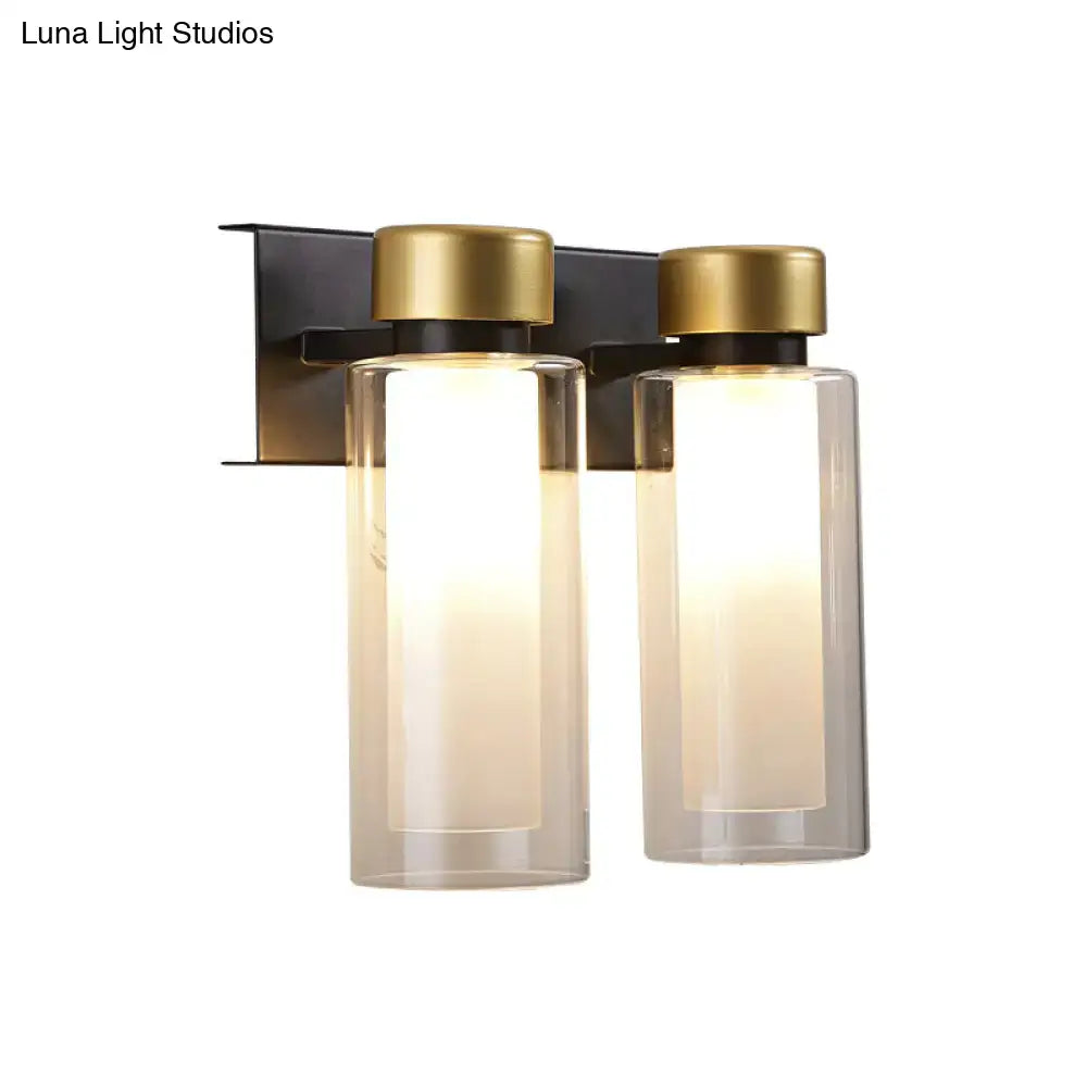 Modern gold and black wall lamp with dual clear glass cylinder shades and gold-finished bulb base on matte black bracket