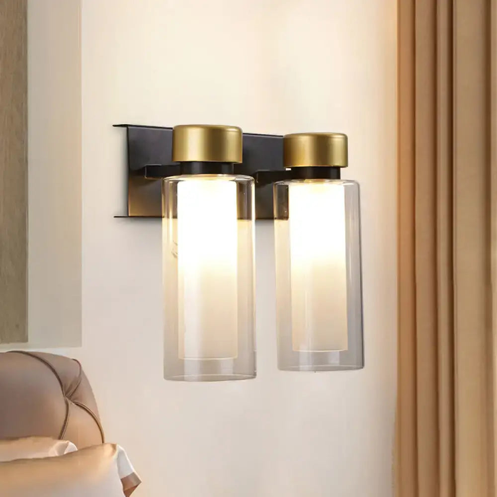 Modern gold and black wall lamp featuring dual clear glass cylinders with gold-toned caps on a matte black bulb base bracket