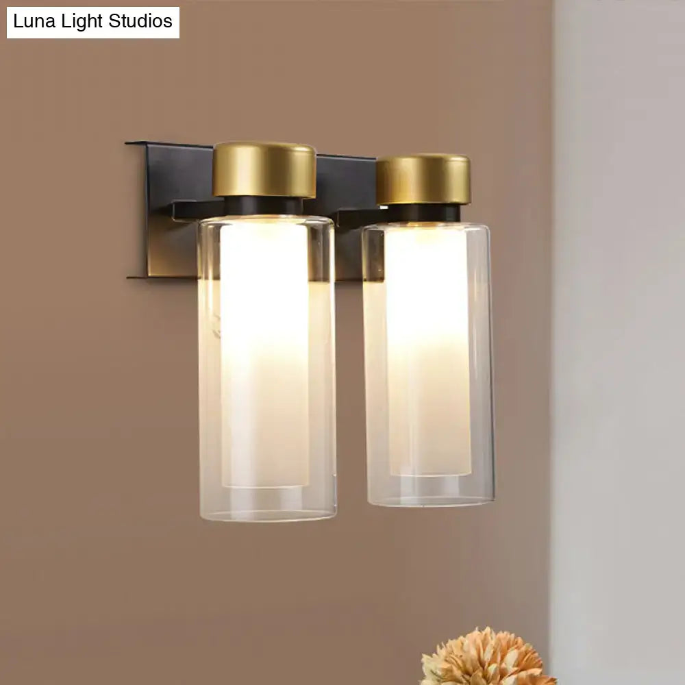 Modern gold and black wall lamp with dual clear cylindrical glass shades and brushed brass bulb base for bedroom lighting