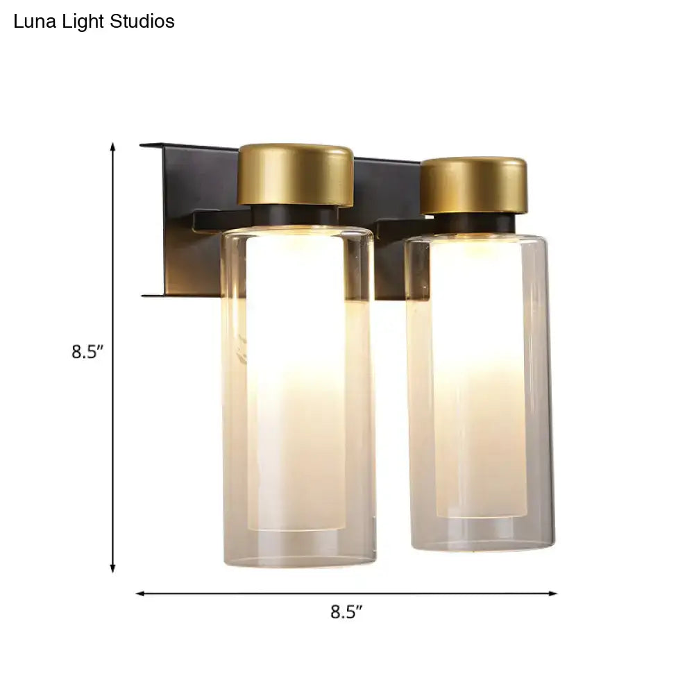 Modern gold and black wall lamp featuring dual frosted glass cylinders with brass tops mounted on black bracket with bulb base