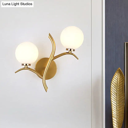 Modern gold branch wall light fixture with two frosted glass shades and leaf-like metal design for living room use