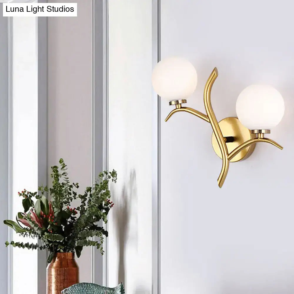 Modern gold branch wall light fixture with two frosted glass globe shades and organic design for living room use