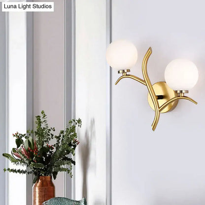 Modern gold branch wall light fixture with two frosted glass globe shades and organic design for living room use