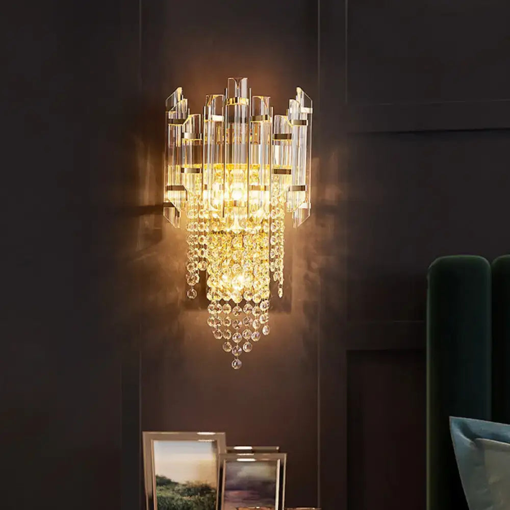 A modern gold clear crystal wall lamp with cascading glass prisms designed as a tiered bedroom wall light