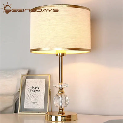 Modern gold crystal ball table lamp with off-white fabric shade and crystal embellishments for bedroom use