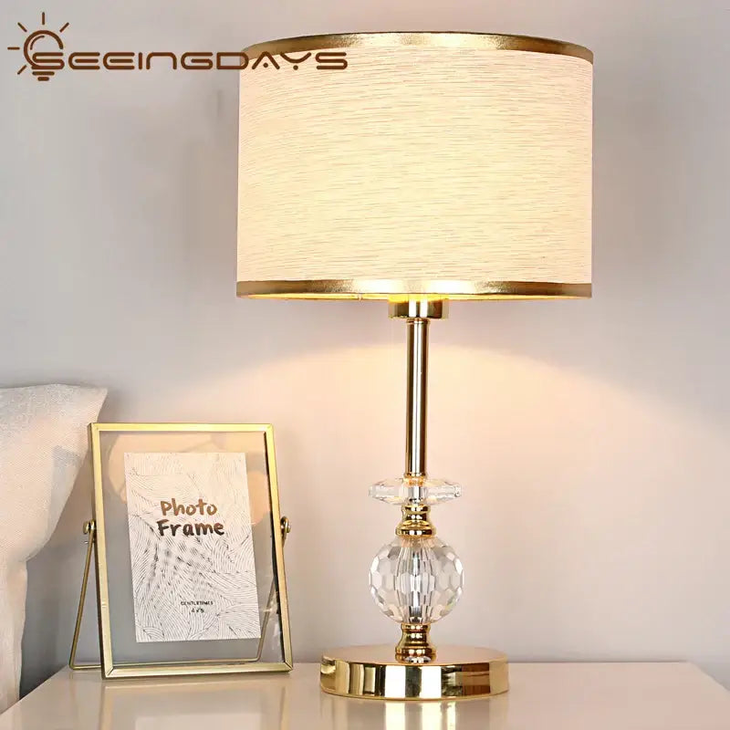 Modern gold crystal ball table lamp with a textured cream fabric shade and crystal accents for bedroom use