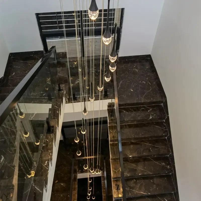 Modern gold crystal bubble chandelier with teardrop pendant above black marble staircase with glass railings decorbites crystal bubble