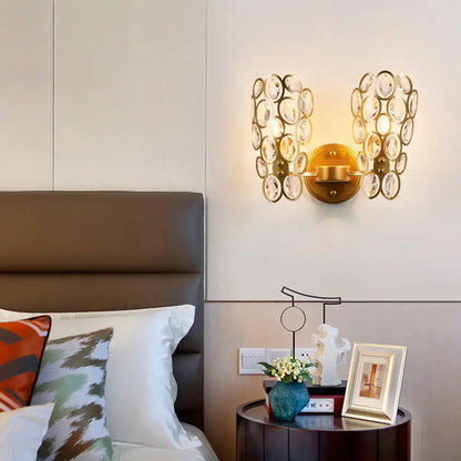 Modern gold wall light featuring a cluster of clear faceted crystal discs arranged in an oval pattern for bedroom use