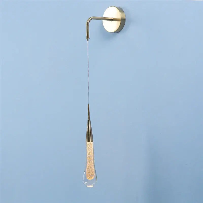 A modern brass-finished wall lamp with a decorbites crystal droplet filled with golden glitter for living room decor