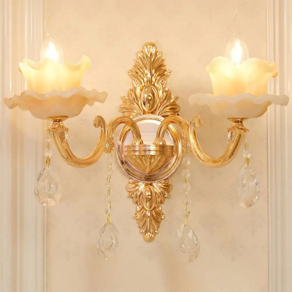 Modern gold wall mount light with ornate design, two candle-style lamps, and crystal droplet accents for bedroom use
