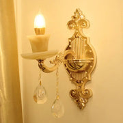 Modern gold wall mount light with ornate curved arm, crystal droplet pendants, and candle-style bulb for bedroom use