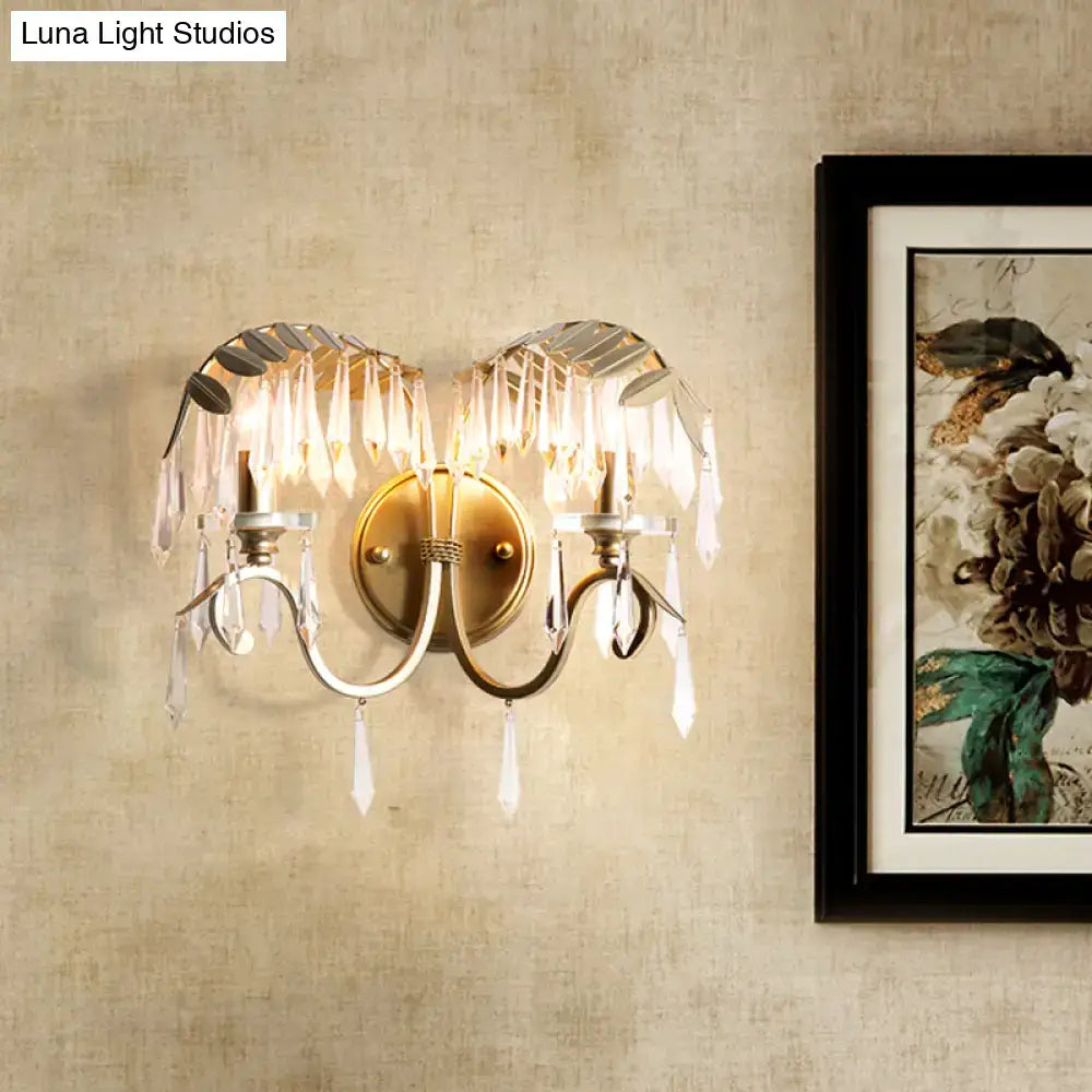 Antique brass wall sconce light with crystal leaf and droplet accents featuring a bent arm design for bedroom use