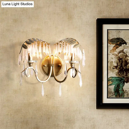 Antique brass wall sconce light with crystal leaf and droplet accents featuring a bent arm design for bedroom use