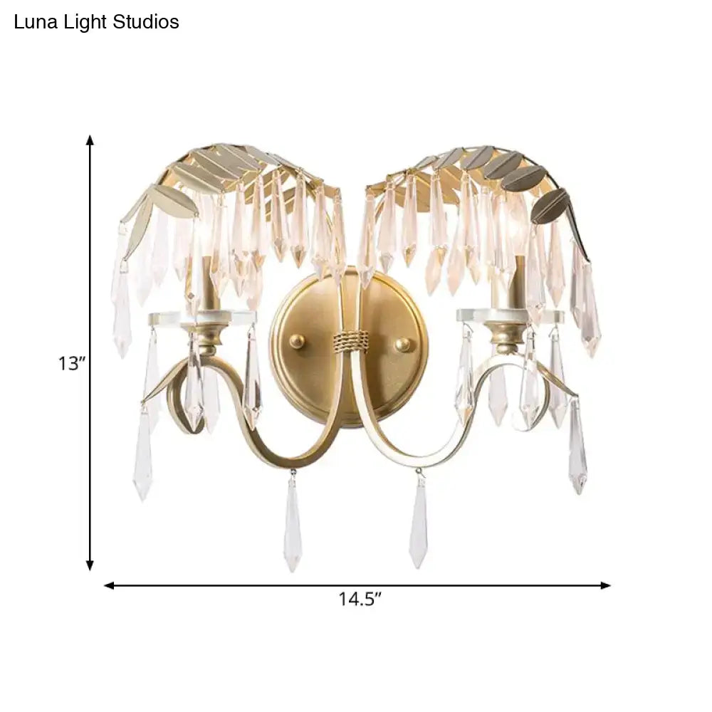 Modern gold wall sconce light with bent arm featuring leaf-shaped metal accents and dangling crystal droplets for bedroom use