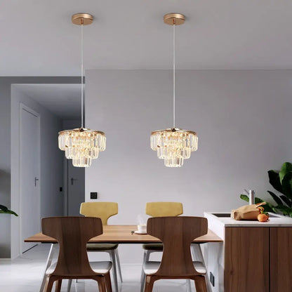 Two elegant gold-toned modern crystal led ceiling chandeliers with cascading crystal tiers for dining room use