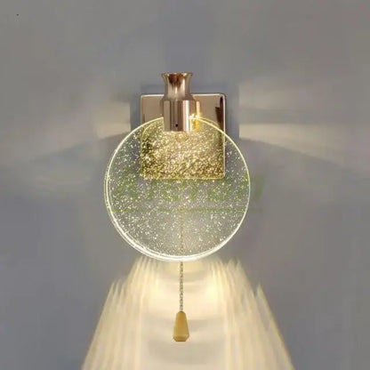 A modern gold crystal led wall lamp with clear glass globe filled with golden glitter and polished brass fixture