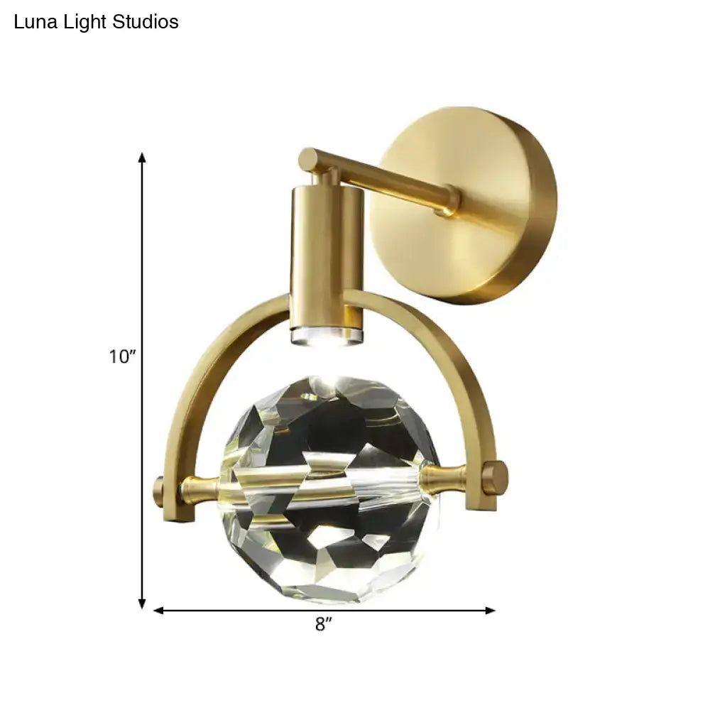 Modern gold led wall lamp with a large faceted crystal globe suspended by an arched brass frame bulb base design