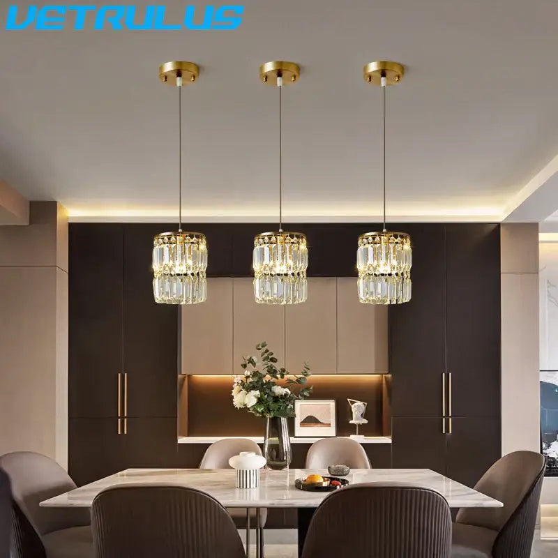 Three elegant gold crystal pendant lights with faceted glass elements hang above a modern dining table