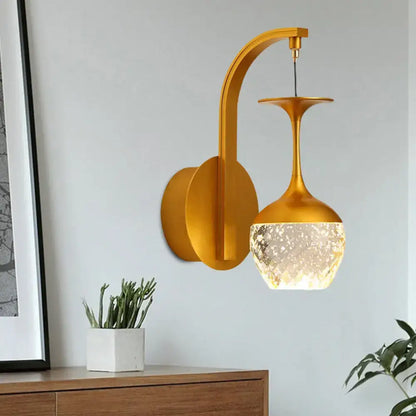 Gold-toned modern wall light with crystal shade featuring curved arm and textured frosted glass for bedroom use