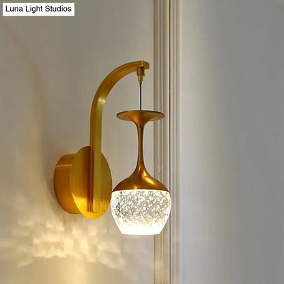 Gold-toned wall light with curved arm and textured frosted crystal shade for modern bedroom sconce lighting