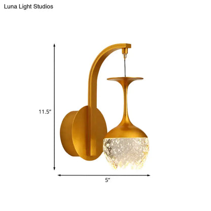 Modern gold wall light with faceted crystal shade designed as an inverted wine glass for bedroom use