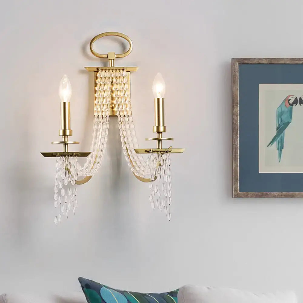 Modern gold crystal strand wall sconce with two candle-style bulbs and cascading crystal strand beads for bedroom lighting