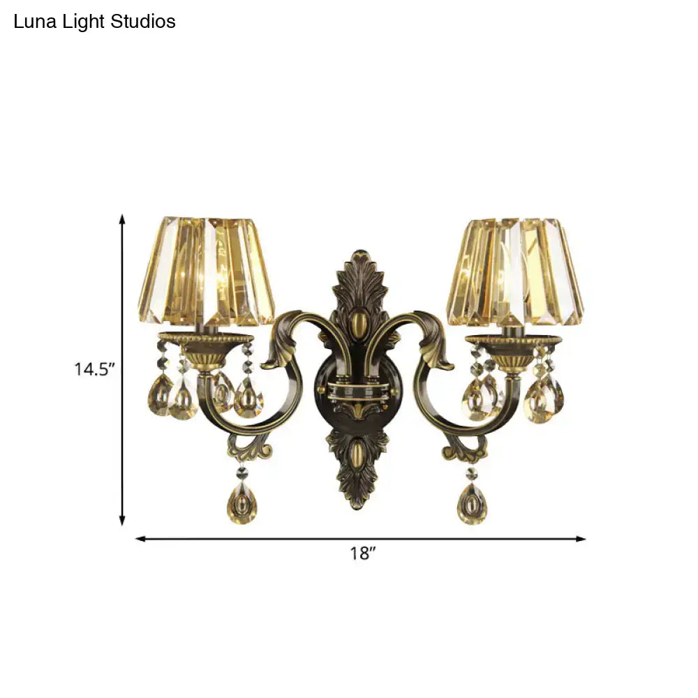 Antique brass two-light wall sconce with faceted amber glass shades and crystal teardrop accents for living room lighting