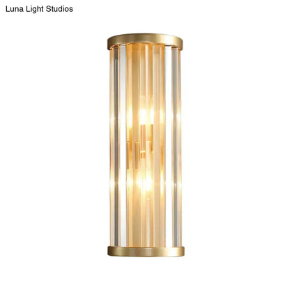 Modern gold crystal wall lamp with two lights featuring gold-toned cylindrical design and vertical clear glass rods glowing warmly