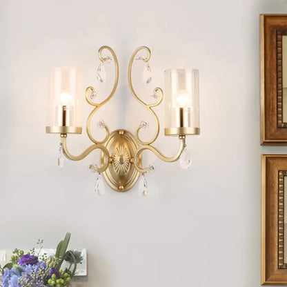 Modern gold wall light with ornate design crystal droplets and clear glass cylinder shade for bedroom use