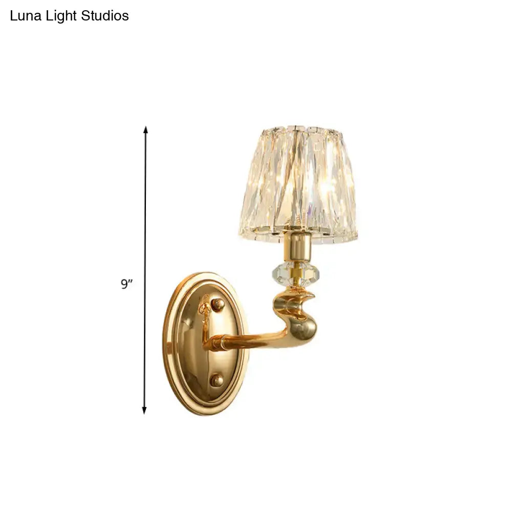 Modern gold wall light fixture with faceted crystal shade and ornate curved arm for bedroom lighting