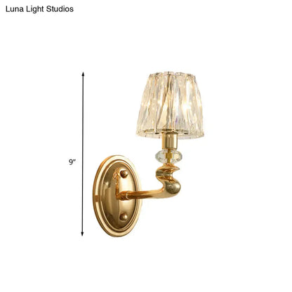 Modern gold wall light fixture with faceted crystal shade and ornate curved arm for bedroom lighting