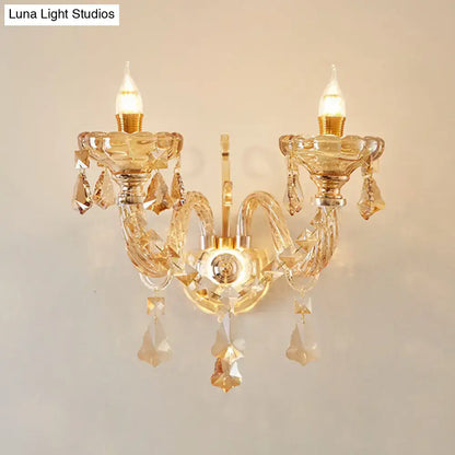 Modern gold crystal wall sconce inch fixture with two candle-style bulbs and dangling faceted crystals for bedroom use