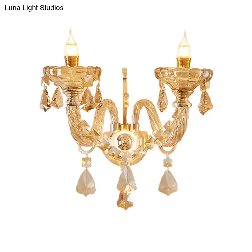 Modern gold crystal wall sconce inch fixture with two lit candle style bulbs and dangling teardrop crystals for bedroom