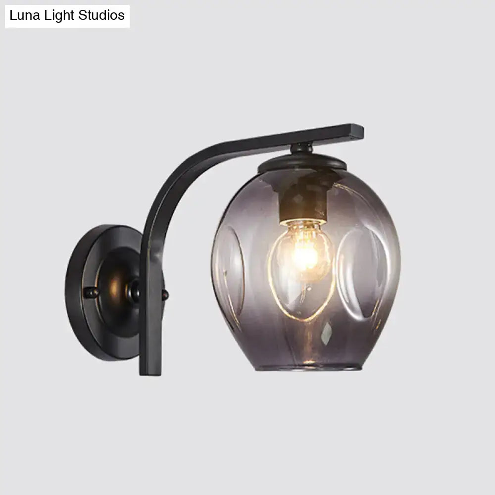 A sleek black metal wall sconce with curved arm and smoked glass globe featuring an exposed filament bulb