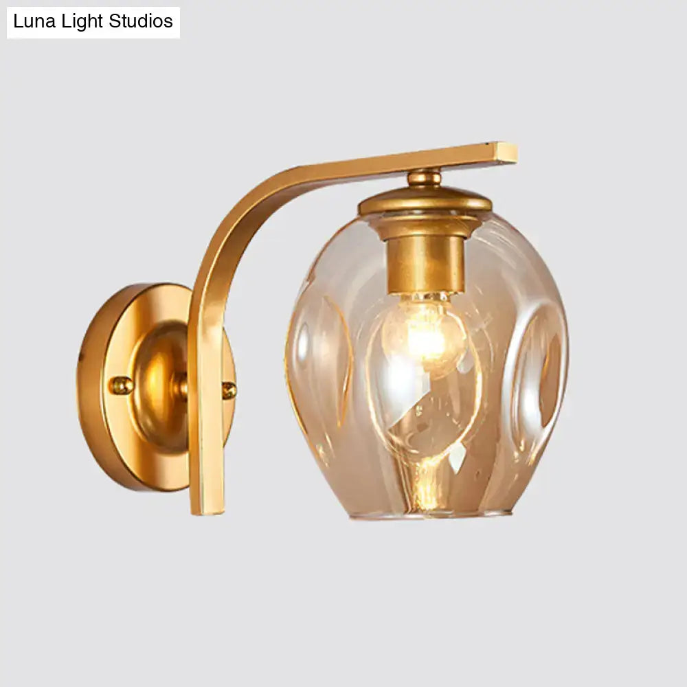 Modern gold curved arm glass wall sconce with textured amber globe and exposed bulb for bedroom lighting