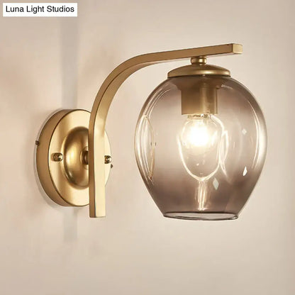 Modern gold curved arm glass wall sconce with warm-toned brass and smoked glass globe for bedroom lighting