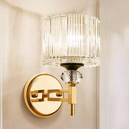 Modern gold cylinder sconce wall lamp with clear vertically ribbed glass and faceted crystal accent for bedroom