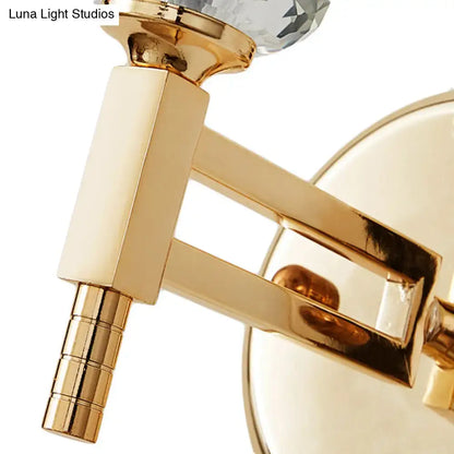 Modern gold cylinder sconce wall lamp featuring a gold-toned finish and faceted crystal accent for bedroom use