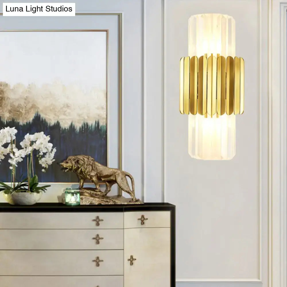 Modern gold cylinder wall mount lamp with vertical fluted glass panels providing warm diffused glow for bedroom use