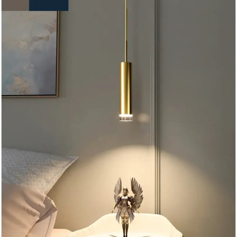 A sleek gold modern led pendant light with a cylindrical design hangs above a small figurine in bedroom decor