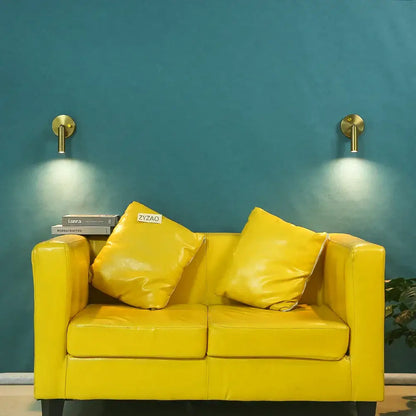 Bright yellow leather sofa with matching cushions under modern gold cylindrical led wall lamp with knob switch