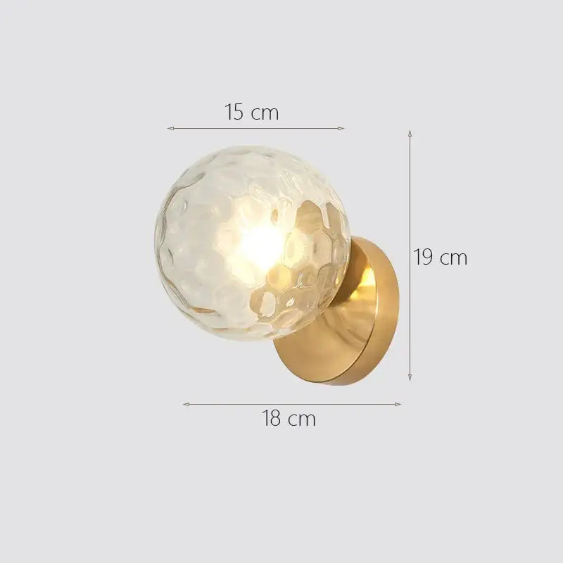 A modern wall lamp featuring a decorbites glass ball with textured translucent glass and polished brass base for bedroom use