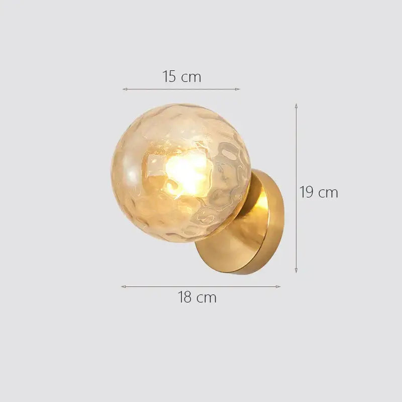Modern gold decorbites glass ball wall lamp featuring a gold-toned brass base and textured amber glass globe bedroom sconce