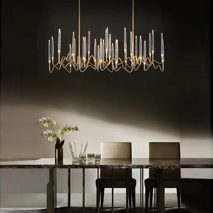 A modern gold elegant candle shape ceiling chandelier with clear glass candle elements and metal arms above dining table