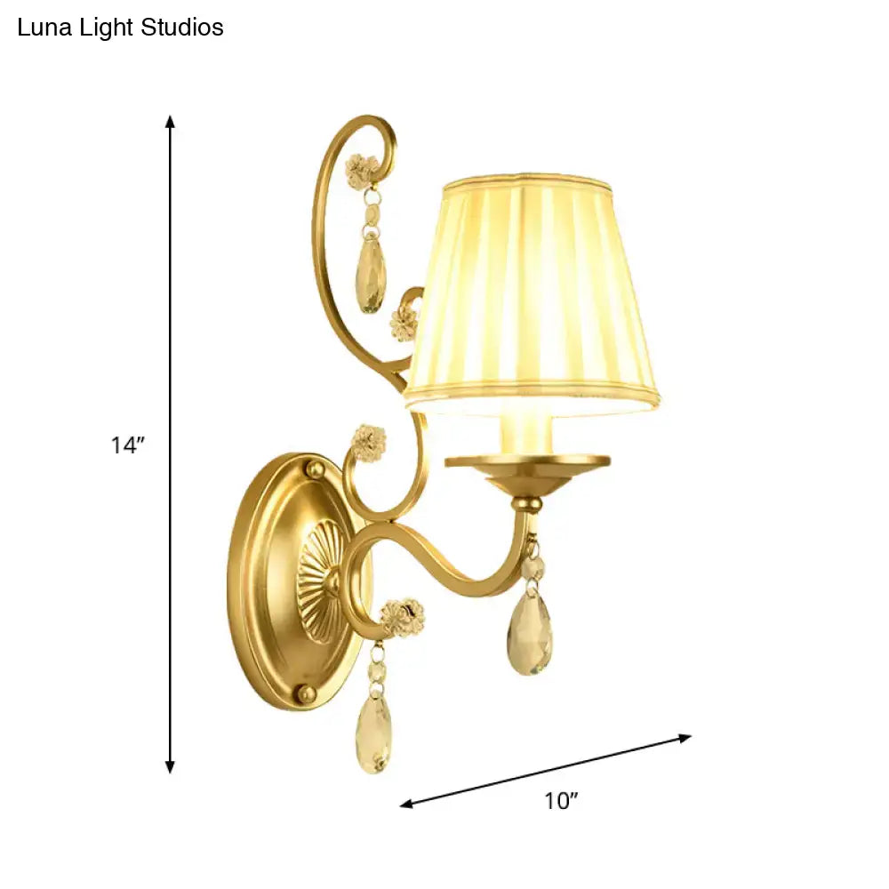 Modern gold fabric wall sconce light fixture with tapered surface, cream pleated shade, and crystal accents for bedroom