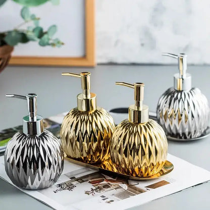 Three elegant modern gold faceted glass liquid soap dispensers with silver and gold pumps on a tray for bathroom decor
