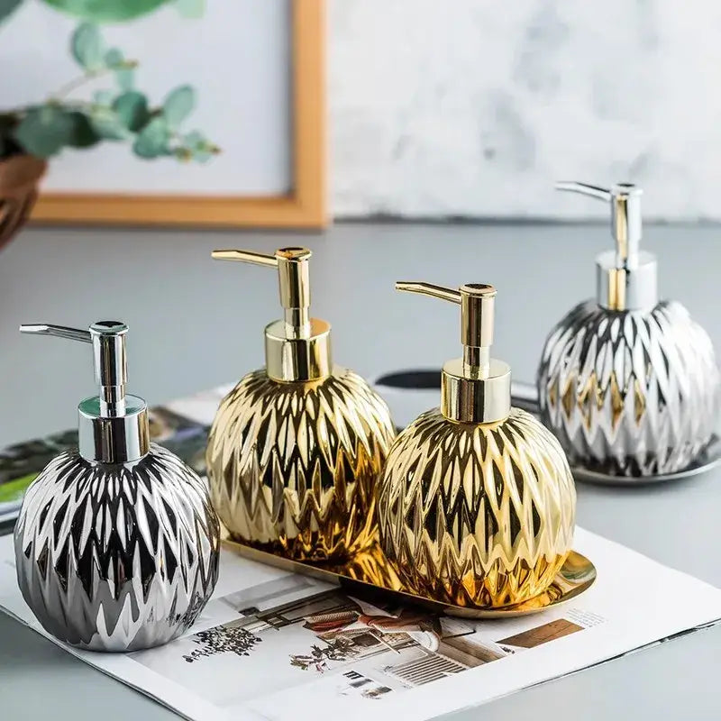 Three elegant modern gold faceted glass liquid soap dispensers with silver and gold pumps on a tray for bathroom decor