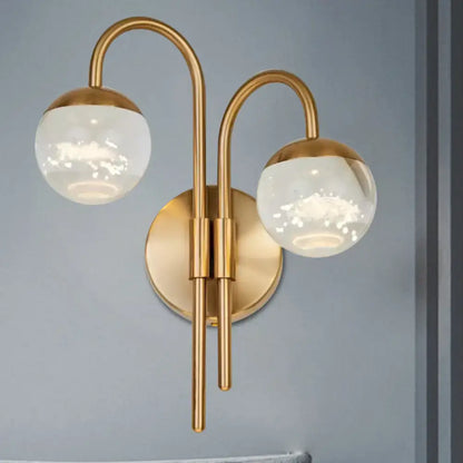 Modern gold finish wall sconce with brass curved arms and frosted crystal globes for living room lighting