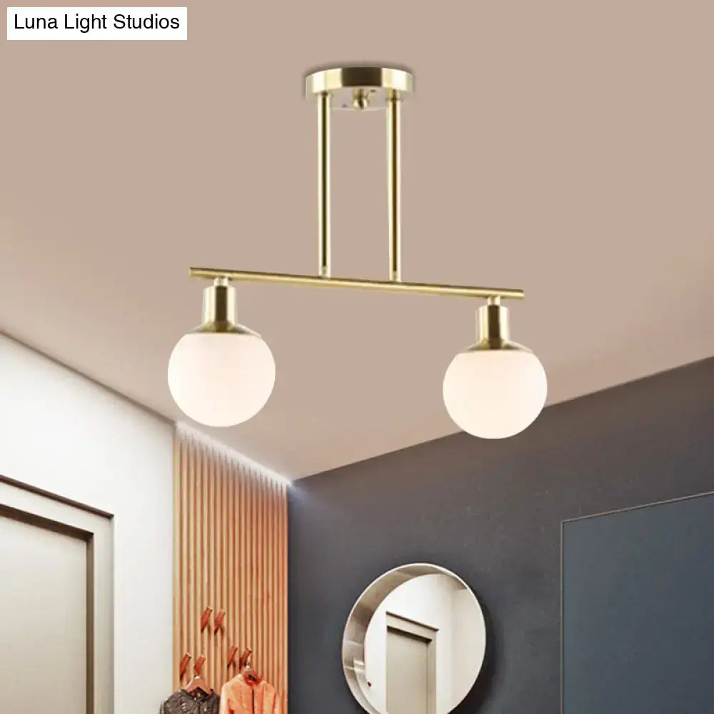 Modern brass-finished linear chandelier pendant light with two spherical milk glass globes and gold finish